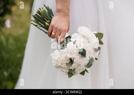 Une mariée accroche délicatement un bouquet de mariage d'œillet blanc luxuriant avec des accents d'eucalyptus, symbolisant l'amour. la mise au point douce et la lumière naturelle créent un r Banque D'Images