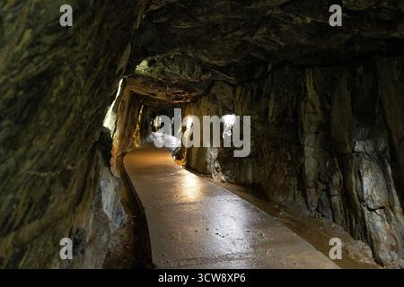Ruskeala Mountain Park long chemin étroit, humide et pavé à l'intérieur d'un tunnel souterrain avec des murs de pierre rugueuse, éclairé par des projecteurs chauds le long de la sid Banque D'Images