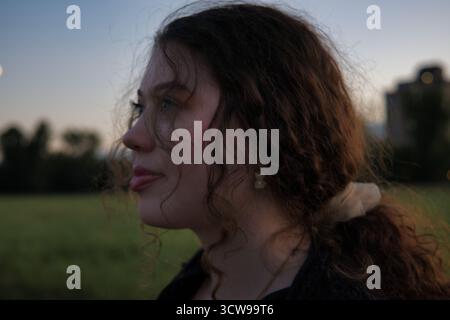 Contemplative jeune femme dans Side Profile au crépuscule avec Ponytail Curly Hair et Moonlit Sky dans Peaceful Outdoor Field pour Reflective Mood et Evening P. Banque D'Images