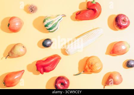 Différents légumes sur fond jaune clair avec des ombres. Citrouilles, maïs, poivrons, tomates, poires et pommes comme concept de récolte d'automne. Haut Banque D'Images
