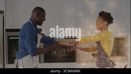 Couple souriant portant des tabliers tenant les mains sur le comptoir blanc dans la cuisine moderne, avec des fours en acier Banque D'Images