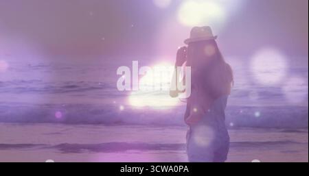 Contempler femme dans la Fedora de paille, combinaisons en denim face à l'horizon à la plage crépusculaire de lentille, espace de copie Banque D'Images