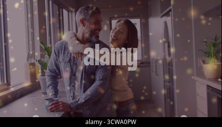 Homme senior souriant tenant une tasse en céramique au comptoir de la cuisine, avec une femme asiatique serrant les épaules Banque D'Images