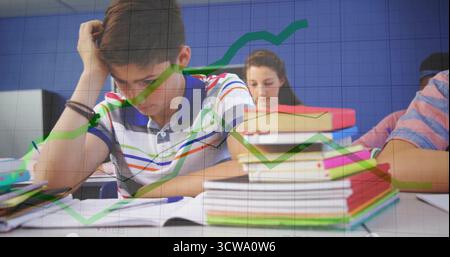 Ecriture garçon dans une chemise rayée penchée sur un cahier en classe, avec des piles de manuels, des lignes de graphique Banque D'Images