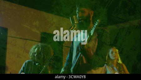 Homme barbu chantant strumming guitare électrique sur scène de club à spots verts, avec chœurs Banque D'Images