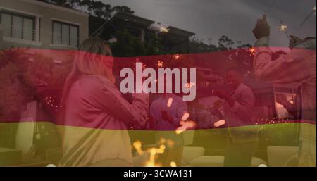 Tenant Sparklers six amis debout autour de la fosse de feu sur le patio au crépuscule, avec des lumières de chaîne Banque D'Images