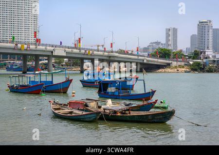 NHA TRANG, VIETNAM - 25 AVRIL 2025. Bateaux de pêche sur la rivière Cai, le pont, gratte-ciel et drapeaux nationaux Banque D'Images