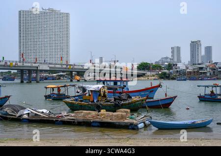 NHA TRANG, VIETNAM - 25 AVRIL 2025. Bateaux de pêche sur la rivière Cai, le pont, gratte-ciel et drapeaux nationaux Banque D'Images