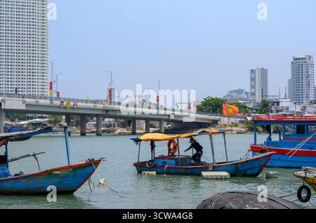 NHA TRANG, VIETNAM - 25 AVRIL 2025. Bateaux de pêche sur la rivière Cai, le pont, gratte-ciel et drapeaux nationaux Banque D'Images