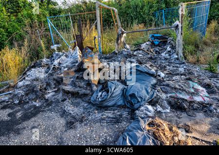 Déchets brûlés et déchets plastiques fondus près d'un chemin industriel clôturé, montrant des déversements illégaux et une pollution urbaine à Vienne Banque D'Images