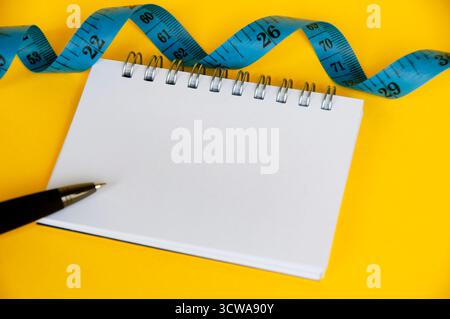 Ruban de mesure diététique avec cahier vierge sur couverture jaune Banque D'Images