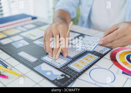 Un concepteur masculin s'est concentré sur les tâches d'interface utilisateur UX, créant des prototypes d'applications avec des éléments filaires, des esquisses et des palettes de couleurs. Il travaille avec des idées créatives pour optimiser Banque D'Images