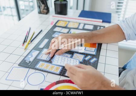 Un concepteur masculin s'est concentré sur les tâches d'interface utilisateur UX, créant des prototypes d'applications avec des éléments filaires, des esquisses et des palettes de couleurs. Il travaille avec des idées créatives pour optimiser Banque D'Images