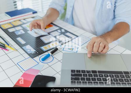 Un concepteur masculin s'est concentré sur les tâches d'interface utilisateur UX, créant des prototypes d'applications avec des éléments filaires, des esquisses et des palettes de couleurs. Il travaille avec des idées créatives pour optimiser Banque D'Images