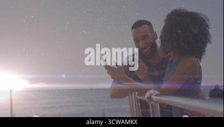 Couple penchant regardant smartphone sur balustrade en métal surplombant l'horizon de l'océan au coucher du soleil, espace de copie Banque D'Images