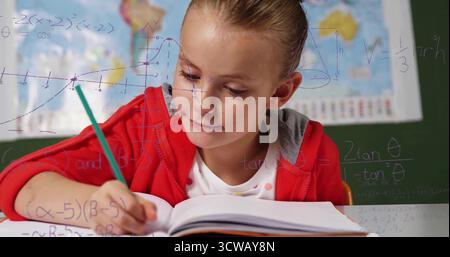 Écriture élève portant un sweat à capuche à l'aide d'un crayon vert au bureau dans la salle de classe, avec cahier et carte du monde Banque D'Images