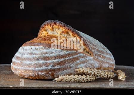 Miche rond de pain au levain fraîchement cuit avec des épis de blé sur une planche à découper en bois, gros plan. Pain rustique au levain. Cuisiner du levain sain Br Banque D'Images