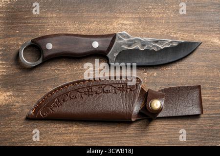 Couteau tranchant forgé fait à la main avec un manche en bois. Couteau en acier de chasse avec étui en cuir, gros plan, vue de dessus Banque D'Images
