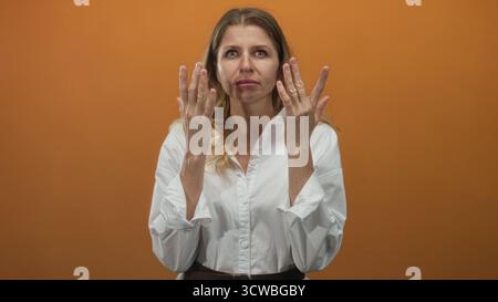 Femme pressant les mains aux yeux frottant le pont de nez dans le studio avec le mur orange portant une chemise blanche ; récupération de fatigue. Banque D'Images