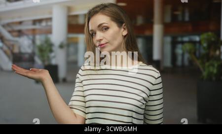 Femme tient la main ouverte paume tournée vers le haut dans le bâtiment moderne spacieux ; question d'incertitude d'enquête de curiosité. Banque D'Images
