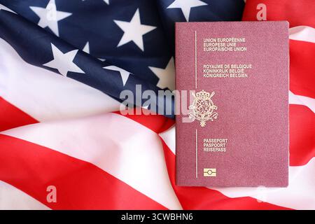 Passeport belge sur grand drapeau agitant des États-Unis d'Amérique close up. Visa AMÉRICAIN et concept d'immigration Banque D'Images