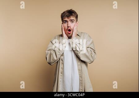 portrait du jeune homme surpris, son expression mettant en évidence les réactions humaines sur fond beige Banque D'Images