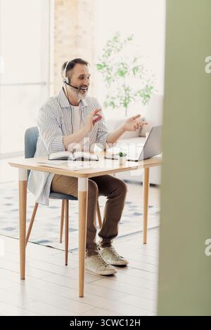 Homme d'affaires mature confiant travaillant à domicile, s'engageant dans des communications en ligne à l'aide d'un ordinateur portable, affichant un comportement professionnel. Banque D'Images