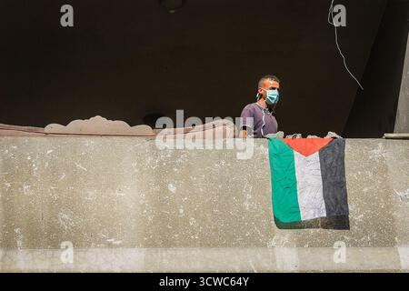 Khan Yunis, Territoires palestiniens. 11 octobre 2025. Un drapeau palestinien pend au balcon d'une maison détruite à Khan Younis, alors que les Palestiniens déplacés rentrent chez eux après le retrait de l'armée israélienne et l'entrée en vigueur du cessez-le-feu. Crédit : Abed Rahim Khatib/dpa/Alamy Live News Banque D'Images