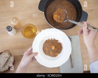 Mains servant soupe de lentilles avec des pommes de terre dans une assiette blanche sur une table en bois, concept d'alimentation saine Banque D'Images