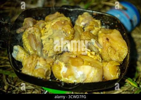 Cette image capture une scène alléchante de morceaux de poulet grésillant dans une poêle en fonte au-dessus d'une flamme nue Banque D'Images