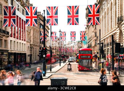 Londres, Royaume-Uni - 14 mai 2018 : scène de rue avec bus à impériale rouge emblématique, drapeaux Union Jack et gens à Piccadilly Circus dans le centre de Lon Banque D'Images