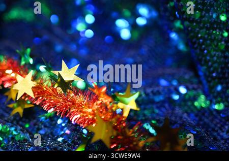 Guirlande brillante avec étoiles dorées et guirlandes rouges sur paillettes bleues scintillantes. Banque D'Images