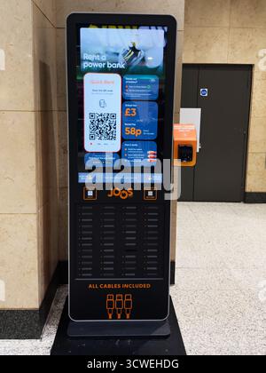 Manchester, Royaume-Uni - 26 septembre 2025 : un grand kiosque numérique Joos offre des chargeurs portables avec codes QR, accès à l'application et paiement par carte dans un couloir. Banque D'Images
