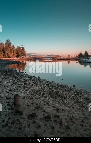 Scène tranquille montre l'eau calme reflétant le ciel du soir avec des arbres bordant le rivage au coucher du soleil, créant une atmosphère paisible. Banque D'Images