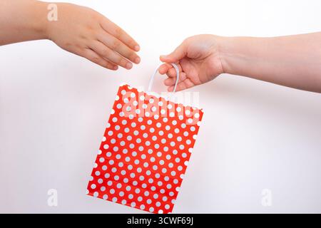 Deux mains échangeant le sac cadeau à pois rouges sur fond blanc isolé. Mains tenant le sac à provisions rouge pointillé. Concept de cadeau et de célébration Banque D'Images