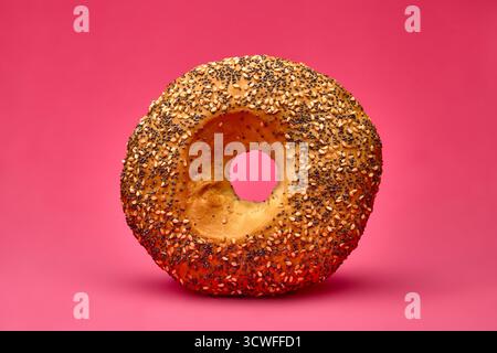 Gros plan d'un petit pain rond parsemé de graines de pavot, isolé sur un fond rose vif. Image parfaite pour la publicité de boulangerie, breakfa Banque D'Images