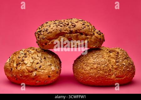 Deux petits pains ronds soutenant un morceau de pain ensemencé sur un fond rose. Disposition alimentaire moderne adaptée à la promotion de la boulangerie et à la conception de l'emballage. Banque D'Images