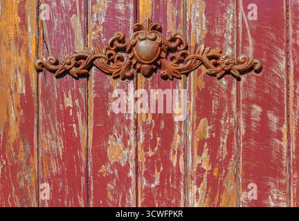 Un gros plan d'une vieille porte de hangar en bois présente une peinture rouge très écaillée, révélant des taches de bois altéré en dessous. Banque D'Images