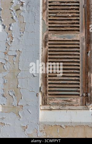 Fenêtre en bois à persiennes dans un bâtiment abandonné affiche une peinture qui s'altère et s'écaille. Le mur adjacent présente une détérioration similaire, avec la Banque D'Images
