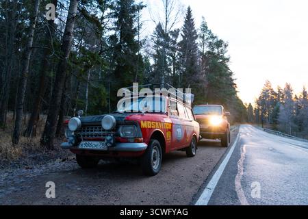 Oblast de Mourmansk, Russie - 13 décembre 2024 : vue de face d'un wagon Moskvich rouge avec phares allumés, garé devant un SUV rouge moderne sur le Banque D'Images