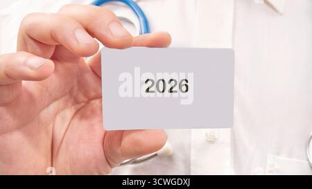 Un médecin en manteau blanc affiche une carte avec 2026 écrit dessus, suggérant une future innovation médicale ou une année d'objectif de soins de santé. Optimisme dans l'ai Banque D'Images