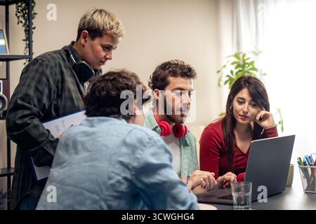 Groupe de jeunes collègues multiethniques qui réfléchissent et analysent des données sur un ordinateur portable lors d'une réunion d'équipe dans un bureau moderne. Banque D'Images