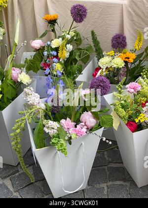 Bouquets de fleurs colorés dans des sacs en papier blanc sur la rue pavée. Photo mobile Banque D'Images