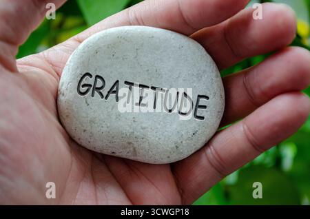 Main tenant une pierre blanche avec un texte DE GRATITUDE gravé dessus, représentant le but de la vie centré sur la reconnaissance et la vie consciente. Banque D'Images