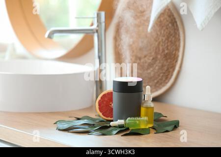 Humidificateur d'air avec des huiles essentielles, feuille de palmier et pamplemousse sur la table dans la salle de bain, gros plan Banque D'Images