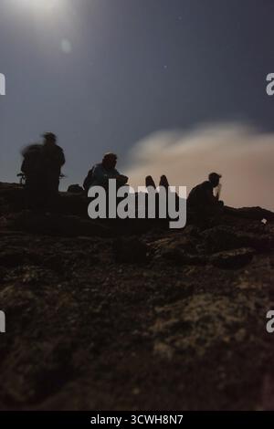 Silhouettes de personnes assises au bord du cratère du volcan Erta Ale, en Éthiopie, en pleine lune Banque D'Images