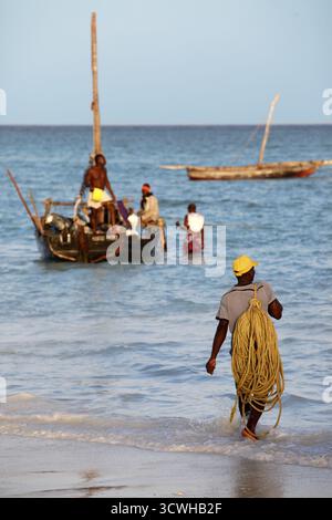 Stone Town (Zanzibar), Tanzanie - 6 janvier 2016 : un boutre (voilier traditionnel) en arrière-plan et un bateau de pêche bondé et un poissonnier dans le foreg Banque D'Images