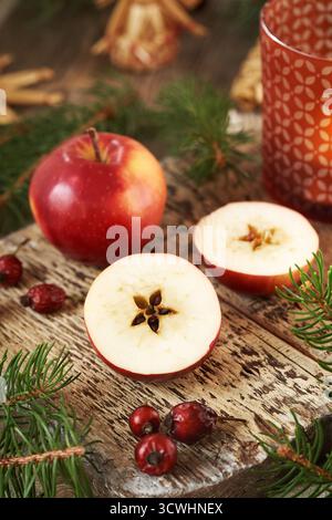 Pomme rouge coupée en deux avec une étoile au milieu, avec décoration de Noël, hanches de rose et branches d'épinette Banque D'Images