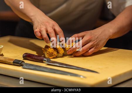 Un chef expérimenté prépare des sushis avec des ingrédients frais sur une planche à découper en bois, mettant en valeur son expertise culinaire et son souci du détail. Banque D'Images