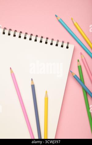 Carnet de croquis et crayons de couleur sur fond rose. Vue de dessus Banque D'Images